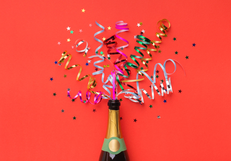 Champagne bottle with colorful party streamers on red backgroundの写真素材