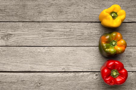 Colorful bell peppers on rustic wooden table. Yellow, green and red paprikas, vegetable meal...