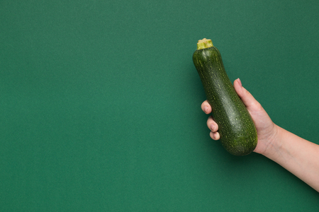 Fresh zucchini in female hand on green background, copy spaceの写真素材