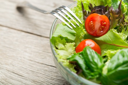 Eating healthy lunch. Fresh green salad with tomatoes in glass bowl with fork, closeup, copy spaceの写真素材