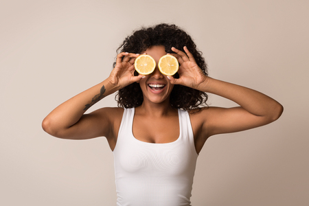 African-american woman with lemon halves near eyes on light backgroundの写真素材