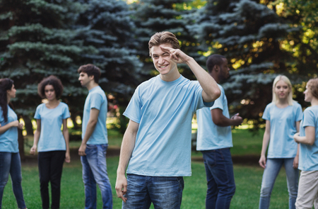 Happy young man volunteer smiling at camera, group meeting in park, copy spaceの写真素材