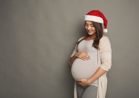 Smiling pregnant woman in Santa hat dreaming about child. Young happy expectant thinking about her baby and enjoying her future life. Christmas birth, pregnancy copy spaceの写真素材
