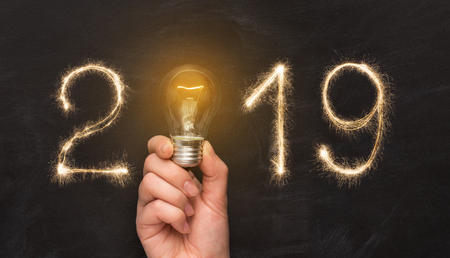 New Year 2019. Man hand holding light bulb with year number over black backgroundの写真素材