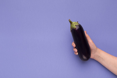 Female hand holding fresh ripe eggplant on purple background, copy spaceの写真素材