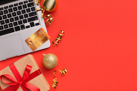 Shopping online for christmas holiday. Laptop with credit card and gift on red background, copy space, top viewの写真素材