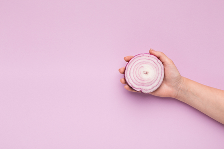 Female hand holding purple onion half on violet background, copy spaceの写真素材