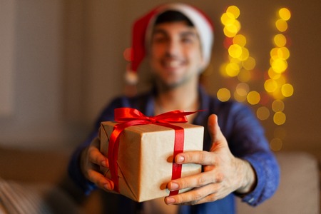 Happy man in santa hat giving present box in home christmas interior