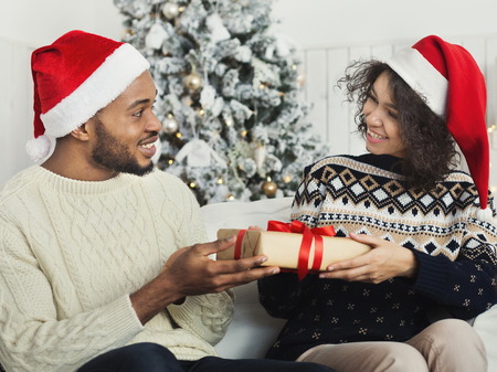 Presenting gifts as Christmas eve tradition. Happy african-american couple exchanging xmas presents, copy spaceの写真素材