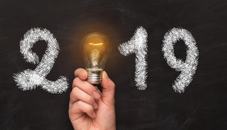 New Year 2019. Man hand holding light bulb with white year number over black background