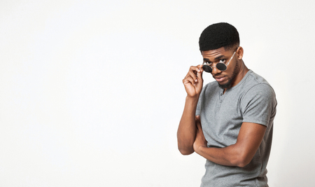 Handsome african-american man adjusting his sunglasses and looking at camera, white studio background, copy spaceの写真素材