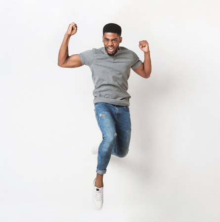 I did it! Handsome african-american man jumping against white background and gesturing with fists