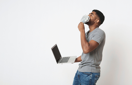 E-commerce and profit online. Young successful african-american man making money from internet at home, holding cash and laptop in hands, copy spaceの写真素材