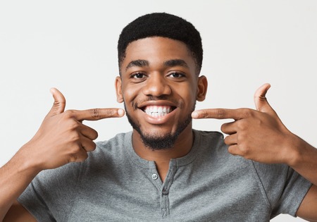 Dental hygiene. African-american man widely smiling and pointing with fingers at his perfect teethの写真素材