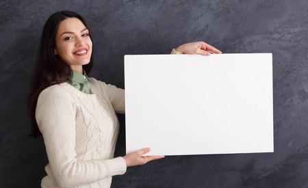 Young successful woman with blank white banner. Smiling girl holding advertising sheet, copy spaceの写真素材