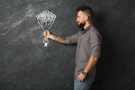 Handsome man giving hand drawn bouquet, standing against black chalkboard in studio.の写真素材