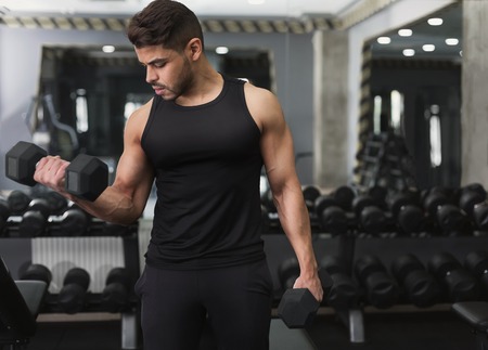 Hispanic muscular man training with dumbbells in modern gym, copy space