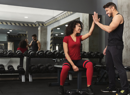 Successful training. Fitness trainer and woman giving each other high five after workout in gym,...
