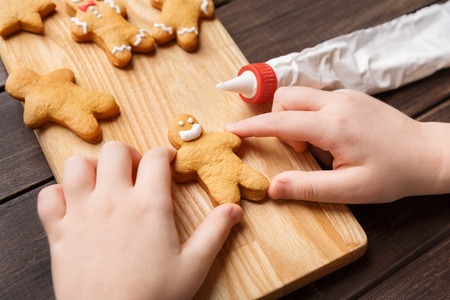 Child decorating homemade gingerbread cookies on wooden board, closeup
