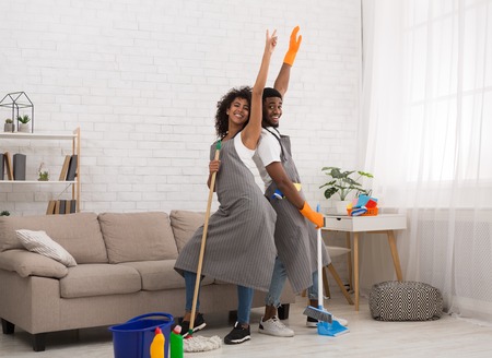 African-american couple staring like on scene while cleaning home with mop and broomの写真素材