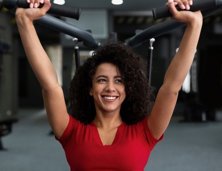 African-american woman exercising at gym, biceps workout on machine