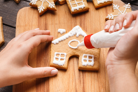 Icing of Christmas bakery. Woman decorating honey gingerbread cookies on wooden board, closeupの写真素材