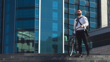 Handsome bearded businessman in classic suit carrying his bicycle while going down the stairs, copy spaceの写真素材