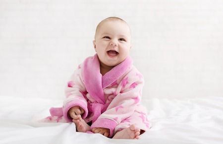 Little cute newborn girl in pink bathrobe laughing on white background, copy spaceの写真素材
