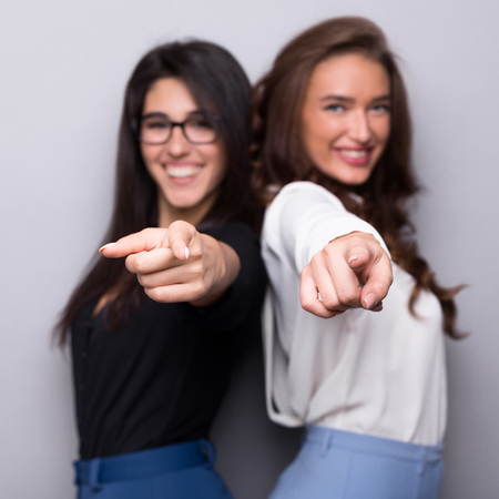 Smiling business women pointing at camera, want you, gray studio backgroundの写真素材