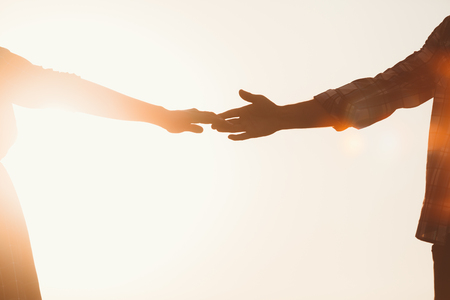Silhouette of lovers hands stretching towards each other against sunset, copy spaceの写真素材