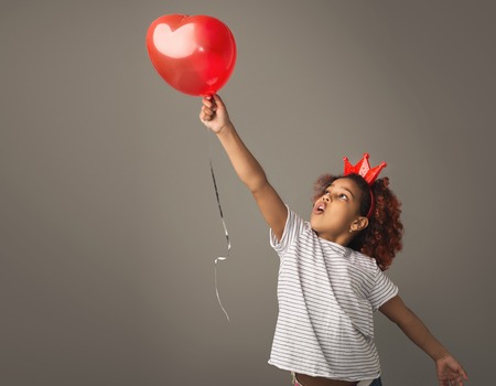 Afro child girl catching balloon on gray backgroung