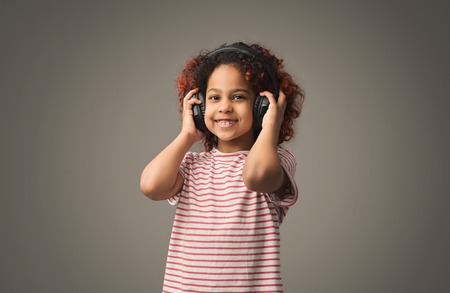 Little black girl in headphones at gray studio backgroundの写真素材
