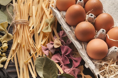 Mixed raw colorful italian pasta with eggs, various vegetables and spices on rustic wooden...