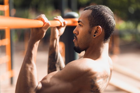 Crossfit man doing pull-ups on chin-up bar during workout outdoors