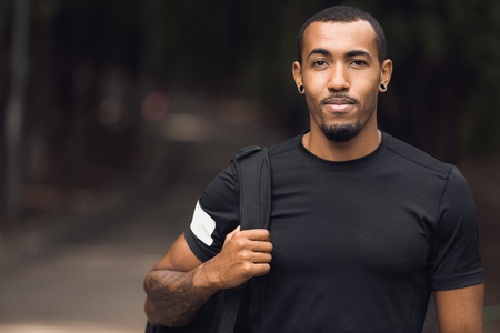 Muscular african-american man wearing black t-shirt and backpack posing outside after workoutの写真素材