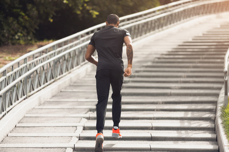 Morning workout. African-american man running up on stairs in summer parkの写真素材