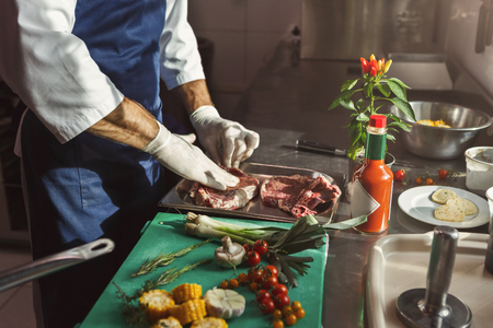 Unrecognizable male chef preparing vegetables for salad, marinating fresh beef steaks at professional hotel or restaurant kitchenの写真素材
