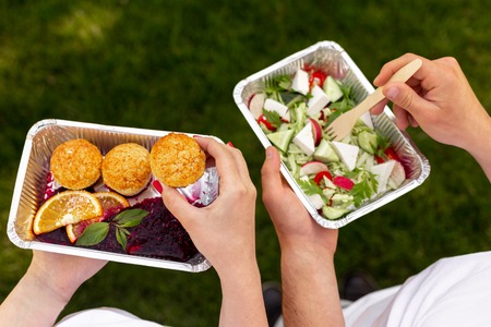 Couple have healthy lunch in park, holding boxes with meal and eating, top viewの写真素材