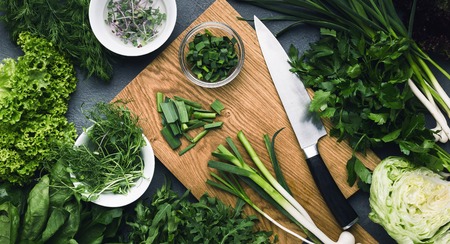 Cutting green spring onion and other greenery on wooden board, top viewの写真素材