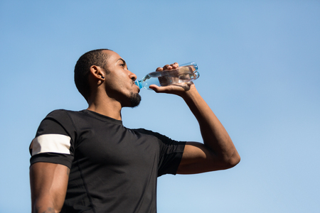 Man resting and drinking water after running over blue sky backgroundの写真素材