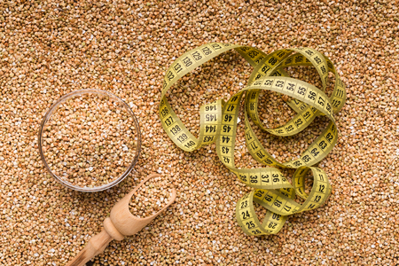 Diet and healthy eating background. Raw buckwheat with wooden spoon and measuring tape, top viewの写真素材