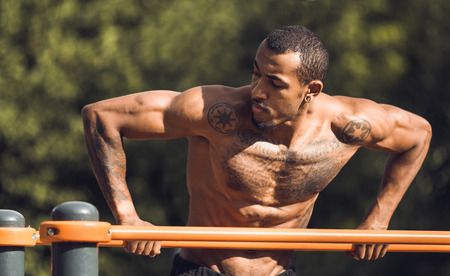 Shirtless african-american athlete doing exercises on parallel bars outdoorsの写真素材