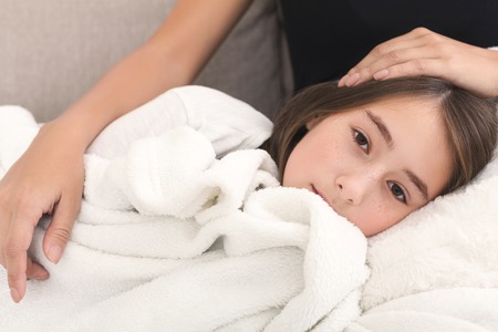 Mother stroking her daughter that lying on moms knees on couch at homeの写真素材