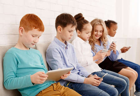 Children and technology. Kids with modern devices sitting near brick wallの写真素材
