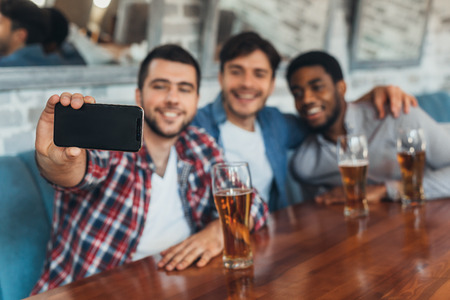 Men taking selfie and drinking beer, sitting in barの写真素材