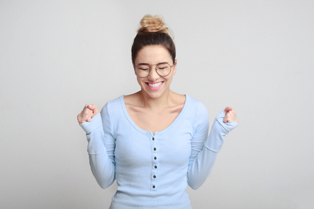 Happy woman with raised hands shouting and celebrating success over gray backgroundの写真素材