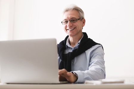 Mature businessman working on laptop, consulting clients at home officeの写真素材