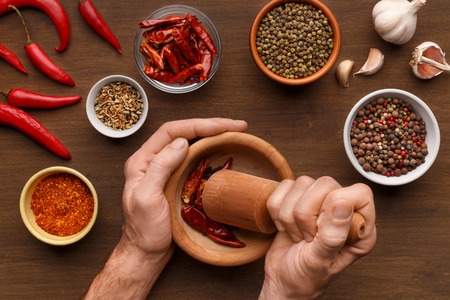 Mans hands grinding spices in mortar, different types of peppercorns and herbs mix on wooden background, top viewの写真素材