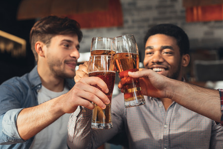 Male friends drinking beer and clinking glasses, enjoying evening at bar