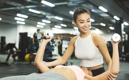Personal trainer helping woman working with dumbbells in sport center